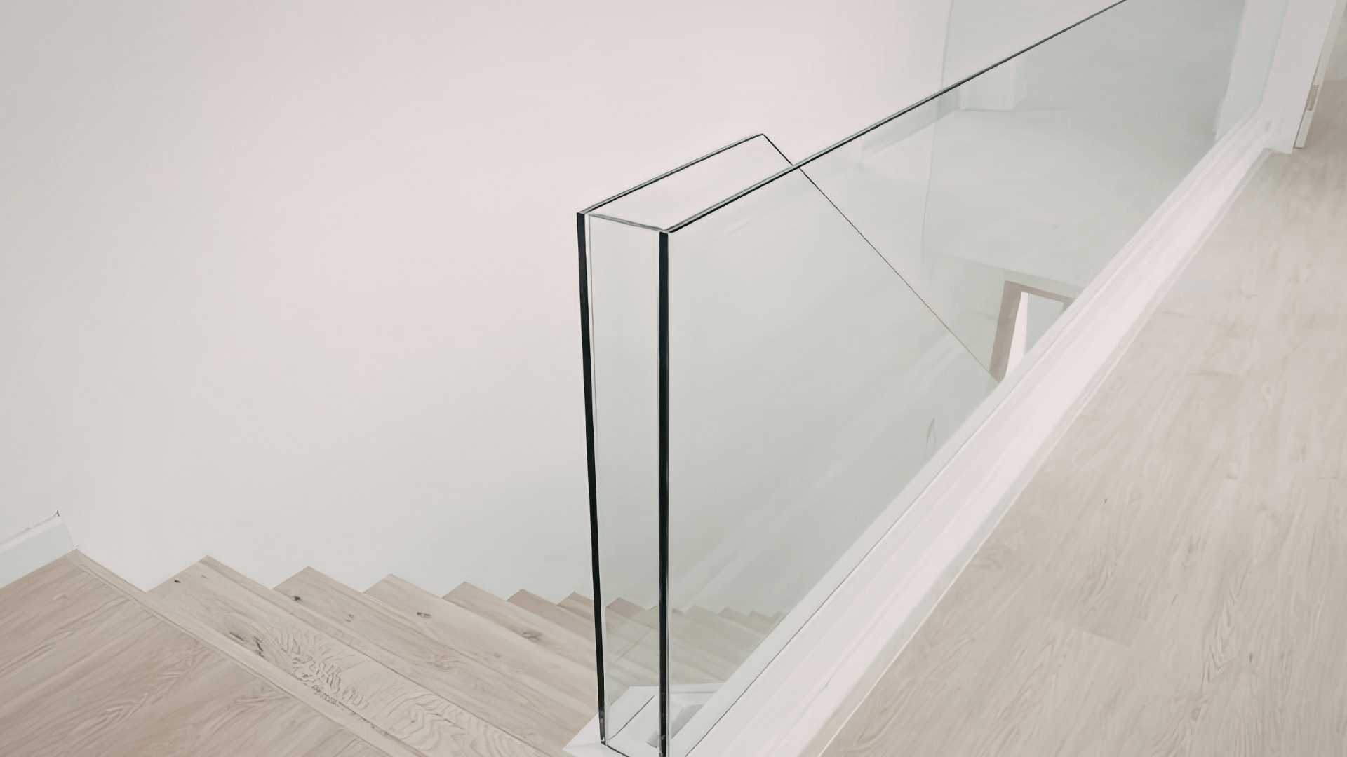 Barandilla de cristal sin postes en escalera interior moderna Barandilla de vidrio continuo tipo “todo cristal” junto a una escalera interior de madera clara, en un espacio minimalista y luminoso.